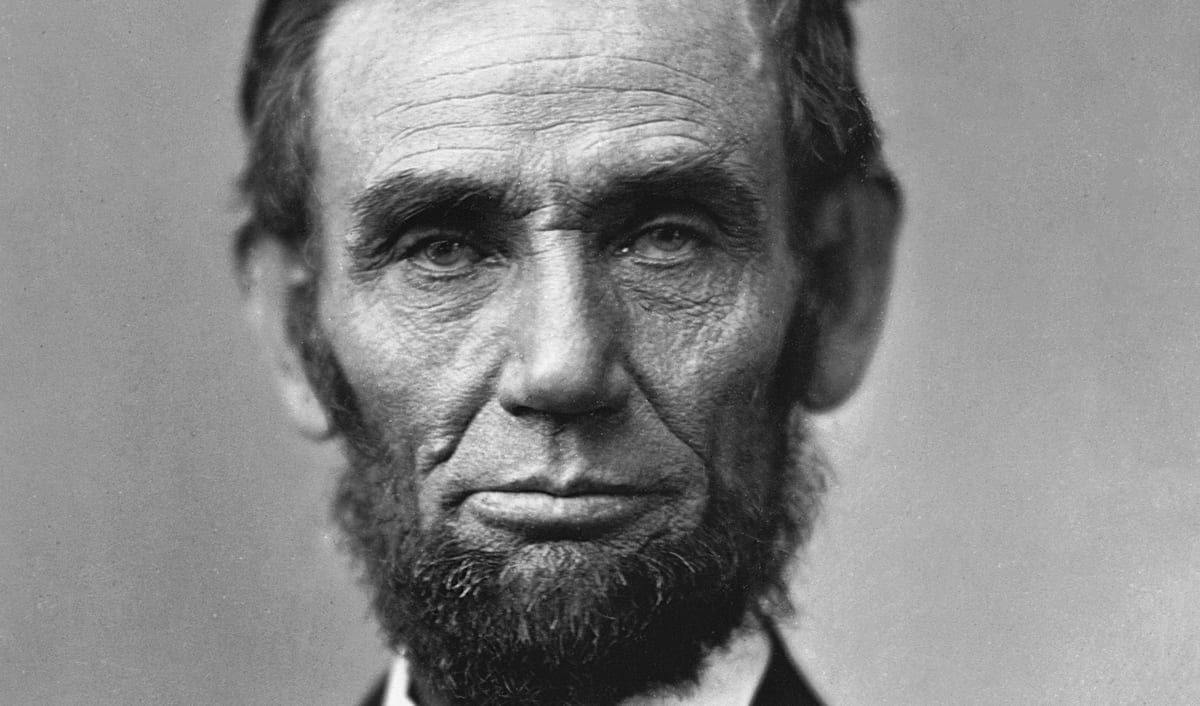 Abraham Lincoln in an 1863 photographic portrait, bearded and in a dark suit, looking straight at the camera.