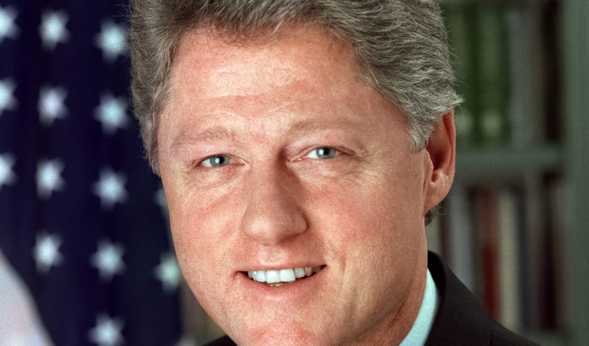 Official White House portrait of Bill Clinton, smiling in a dark suit with the American flag behind him.