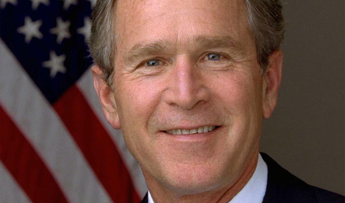 Official presidential portrait of George W. Bush, smiling in a dark suit with the American flag behind him.