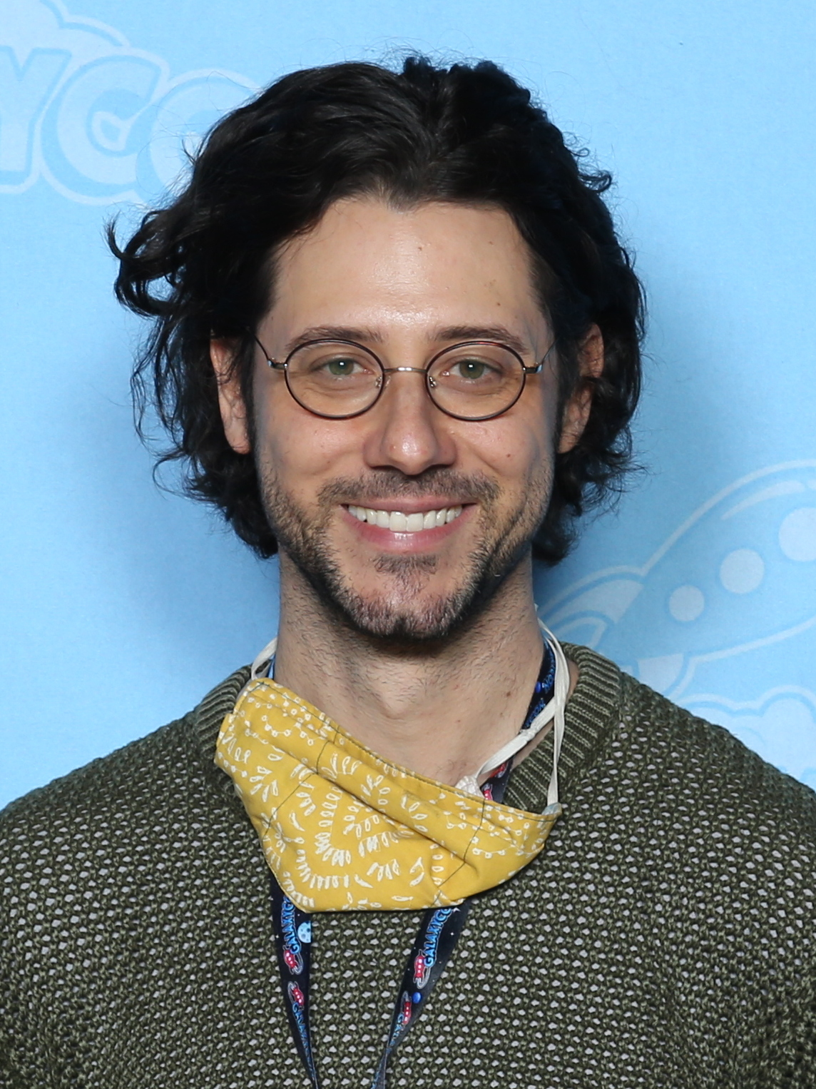 Hale Appleman smiling at a GalaxyCon Richmond photo op in March 2022, wearing glasses and an olive sweater with a mask pulled down around his neck.