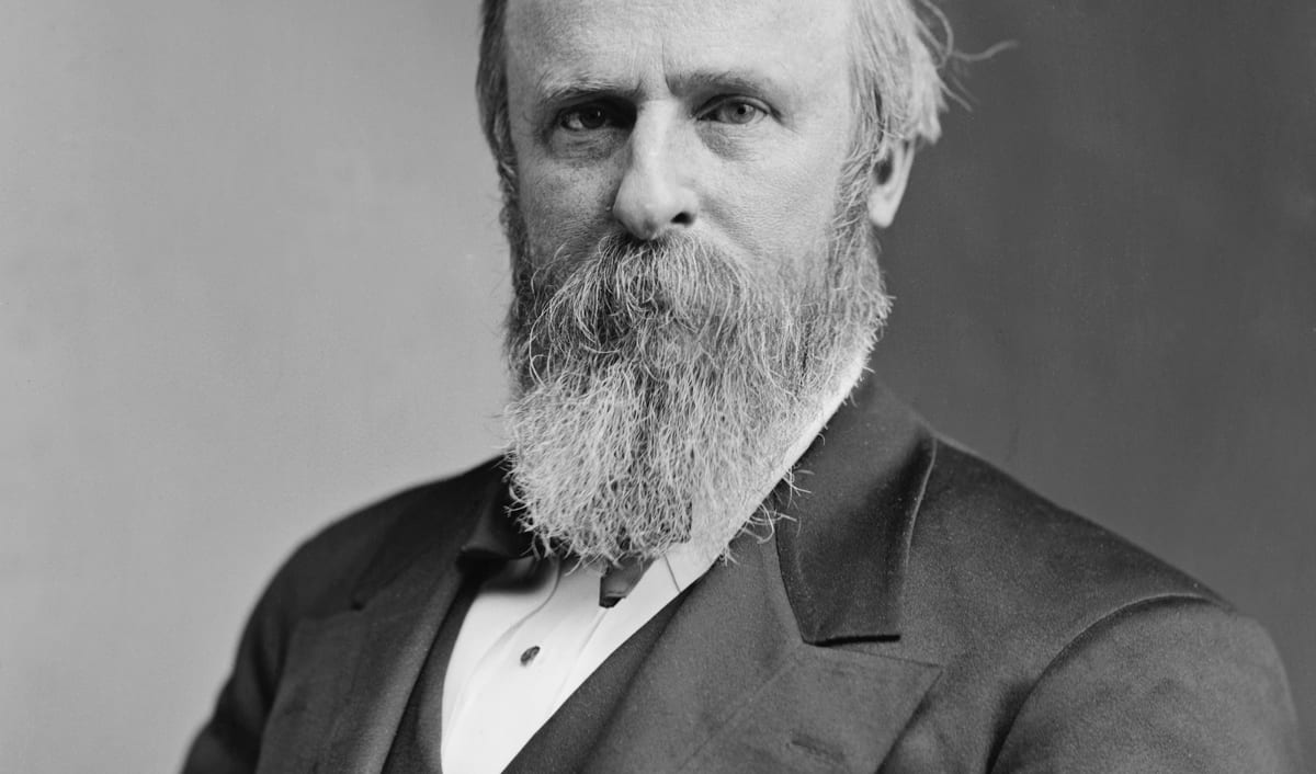 Rutherford B. Hayes photographed in the 1870s, with a full beard and a dark coat.