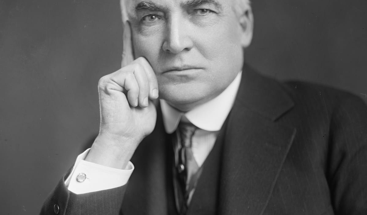 Warren G. Harding in a 1920s portrait photograph, seated with his hand raised to his chin.